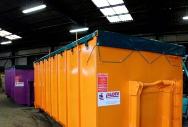 Orange und lila Abfallcontainer mit Planen in einer Lagerhalle.