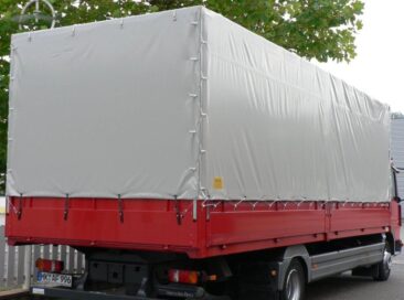 Roter Lkw mit grauem Planenaufbau, der die Ladefläche abdeckt.