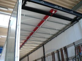 Innenansicht eines Lkw-Aufliegers mit einer roten Rohrstruktur an der Decke und weißen Wänden.