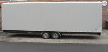 Ein Lkw-Anhänger mit einer grauen Plane, die den Inhalt schützt und abdeckt.