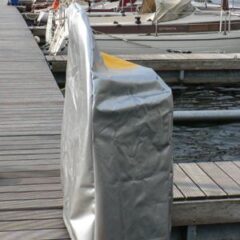 Abgedeckte Bootsausrüstung in silberner Plane am Hafen auf einem Holzsteg.