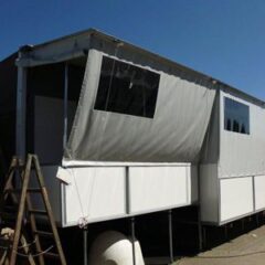 Modularer Wohncontainer mit grauer Markise und Fenstern auf einer Baustelle.