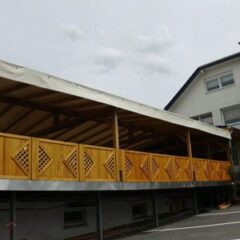 Holzveranda mit einem schrägen Dach und einem dekorativen Geländer aus Holzlatten.