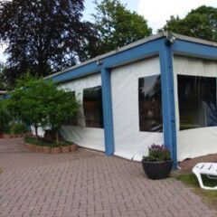Blauer Pavillon mit weißen Seitenwänden und großen Fenstern in einem Gartenbereich.