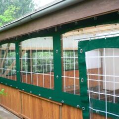 Holzstruktur mit grünen Netzpaneelen und transparenten Folien an einer Wand.