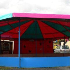 Ein Karussell mit einem bunten Dach in Pink und Blau, ohne Fahrgäste und in einem leeren Zustand.